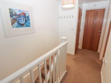 A hallway with stairs and three wooden doors with a painting of boats on the wall at Wood Cottage in Solva