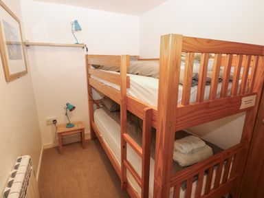 A small bedroom with wooden bunk beds a small table with a lamp a framed picture on the wall and folded towels on the lower bunk at Wood Cottage in Solva