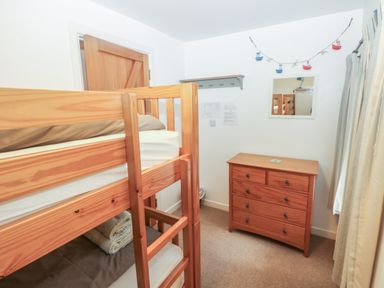 A bedroom with wooden bunk beds a wooden chest of drawers a mirror and a curtain at Wood Cottage in Solva