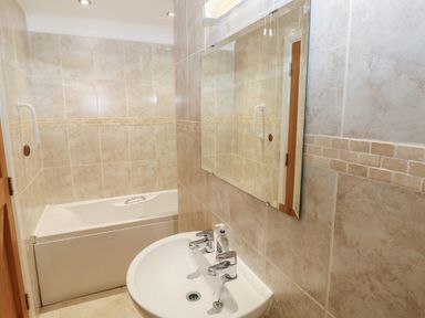 A bathroom with a white bathtub and a sink with two taps and a mirror above it at Wood Cottage in Solva