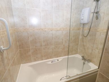 A bathroom with a bathtub shower unit and tiled walls at Wood Cottage in Solva