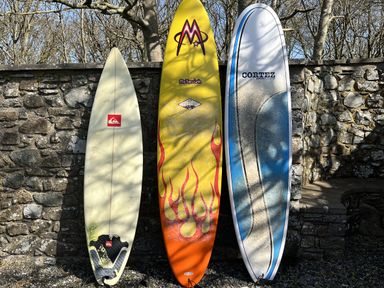 Three surfboards standing vertically against a stone wall outdoors at Wood Cottage in Solva