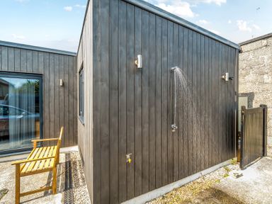 An outdoor shower and wooden bench at Palm House in Newquay