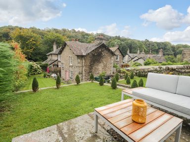 A garden with a sofa and table and stone houses in the background at Pear Tree Cottage in Grange-Over-Sands