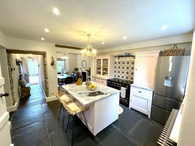 A kitchen with an island, bar stools, a stove, cabinets, and a refrigerator at Pear Tree Cottage in Grange-Over-Sands