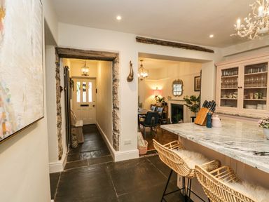 A kitchen with marble countertop and wicker bar stools and a hallway leading to a front door at Pear Tree Cottage in Grange-Over-Sands