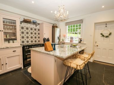 A kitchen with an island countertop with bar stools and a window with view at Pear Tree Cottage in Grange-Over-Sands