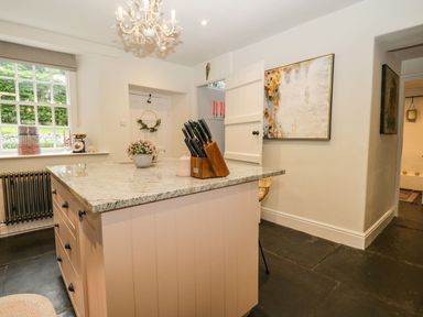 A kitchen with an island featuring granite countertop a knife block and a plant near a window at Pear Tree Cottage in Grange-Over-Sands