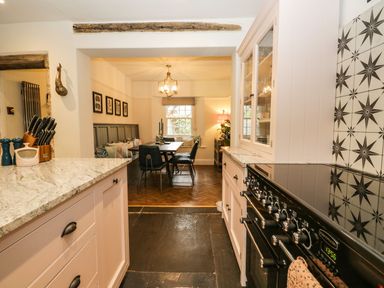 A kitchen with a black stove and white cabinets leading to a dining area with a wooden table and chairs at Pear Tree Cottage in Grange-Over-Sands