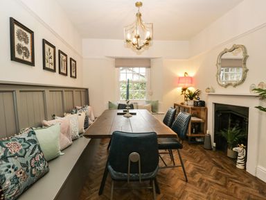 A dining room with a wooden table black chairs a bench with cushions a fireplace and a window at Pear Tree Cottage in Grange-Over-Sands