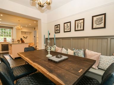 A dining area with a wooden table black chairs cushioned bench and botanical prints on the wall at Pear Tree Cottage in Grange-Over-Sands