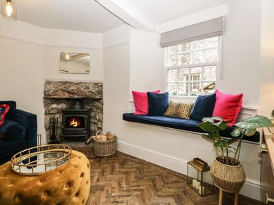 A sitting area with a fireplace a cushioned window seat with pillows and a potted plant at Pear Tree Cottage in Grange-Over-Sands