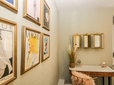 A corner with framed Vogue magazine covers on the wall and a marble top desk with a mirror and decorative plants at Pear Tree Cottage in Grange-Over-Sands