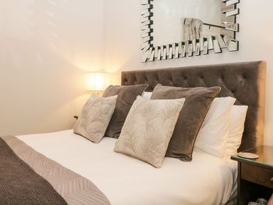 A bed with multiple pillows a lamp and a decorative mirror above the headboard at Pear Tree Cottage in Grange-Over-Sands
