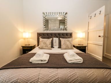 A bedroom with a bed centered between two nightstands with lamps and a decorative mirror above the headboard at Pear Tree Cottage in Grange-Over-Sands