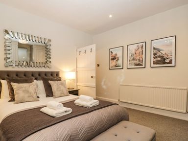 A bedroom with a bed having multiple pillows and folded towels with a mirror above it and framed pictures on the wall at Pear Tree Cottage in Grange-Over-Sands