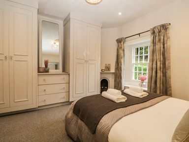 A bedroom with a bed folded towels wardrobe mirror curtains and a window at Pear Tree Cottage in Grange-Over-Sands