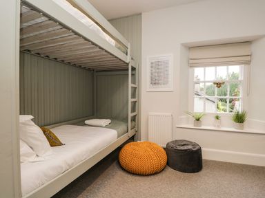 A bedroom with bunk beds pouf seats a window with plants and a framed picture on the wall at Pear Tree Cottage in Grange-Over-Sands