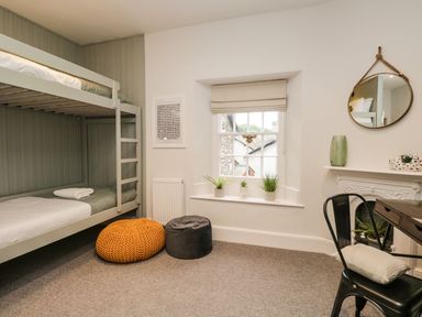A bedroom with bunk beds cushions plants on windowsill a round mirror and a chair at Pear Tree Cottage in Grange-Over-Sands