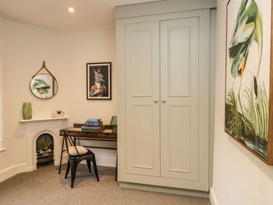 A small office area with a wooden desk and two black chairs near a white fireplace and a large cabinet in a room at Pear Tree Cottage in Grange-Over-Sands