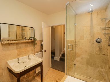 A bathroom with a double sink vanity a mirror a glass shower enclosure and an open door at Pear Tree Cottage in Grange-Over-Sands