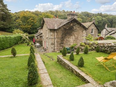 A garden with small trees and stone walls around a stone house at Pear Tree Cottage in Grange-Over-Sands