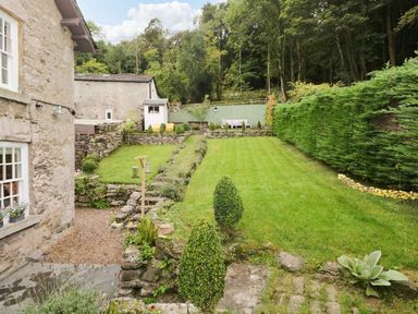 A garden with a lawn and stone walls next to a stone house at Pear Tree Cottage in Grange-Over-Sands