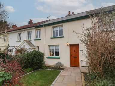 A row of connected houses with white walls green window frames a wooden front door and a small garden path at Sunnymead in Bickington near Barnstaple