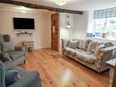 A living room with a patterned sofa two armchairs a wall mounted television wooden door and wood flooring at Sunnymead in Bickington near Barnstaple