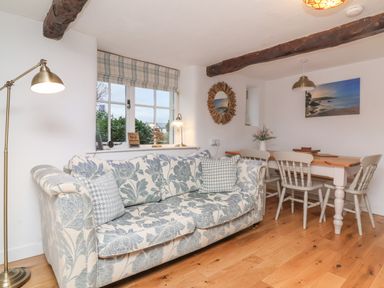 A living room with a floral sofa a dining table with chairs and a window with checkered curtains at Sunnymead Bickington near Barnstaple