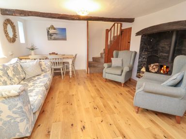 A living room with a fireplace wooden floor a sofa armchairs a dining table chairs and a staircase at Sunnymead in Bickington near Barnstaple