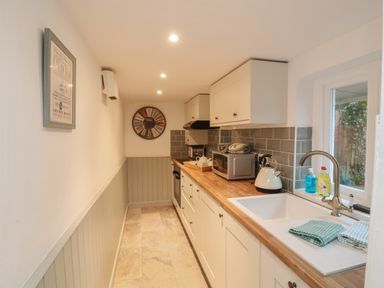 A narrow kitchen with wooden countertops a white sink microwave kettle and a window at Sunnymead in Bickington near Barnstaple