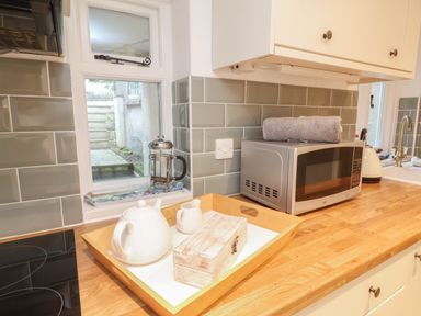 A kitchen countertop with a microwave, a kettle, a wooden tray holding a teapot, a small pitcher, and a wooden box at Sunnymead in Bickington near Barnstaple