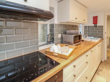 A kitchen with a wooden countertop an electric stove a microwave a sink a French press and kitchen cabinets at Sunnymead in Bickington near Barnstaple