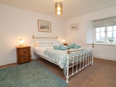 A bedroom with a metal bed frame two bedside tables with lamps a window and a blue rug at Sunnymead in Bickington near Barnstaple