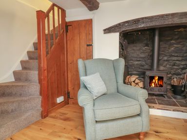 A sitting area with a gray armchair next to a wood burning stove and stairs with a wooden door under the stairs at Sunnymead in Bickington near Barnstaple