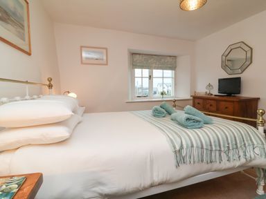 A bedroom with a bed with folded towels and a striped blanket a wooden dresser with a lamp and television and a window with a patterned blind at Sunnymead Bickington near Barnstaple