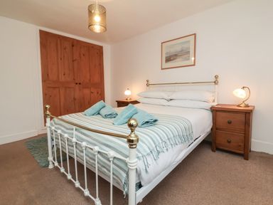 A bedroom with a bed covered with striped blanket and towels bedside tables with lamps and wooden wardrobe at Sunnymead in Bickington near Barnstaple