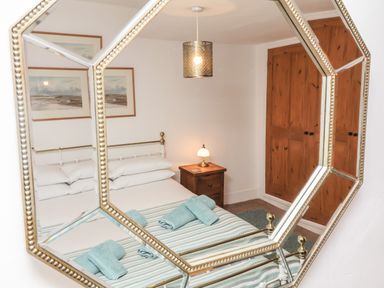 A bedroom with a bed with folded towels bedside table with lamp and wooden closet reflected in a decorative mirror at Sunnymead in Bickington near Barnstaple