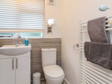 A bathroom with a toilet sink cabinet trash can and towel rack with towels at Sunnymead in Bickington near Barnstaple