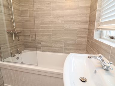 A bathroom with a bathtub a showerhead a sink and tiled walls at Sunnymead in Bickington near Barnstaple