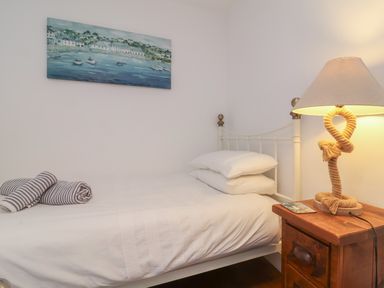 A bedroom with a single bed with white bedding and pillows a wooden nightstand with a rope lamp and a painting of boats on the wall at Sunnymead in Bickington near Barnstaple