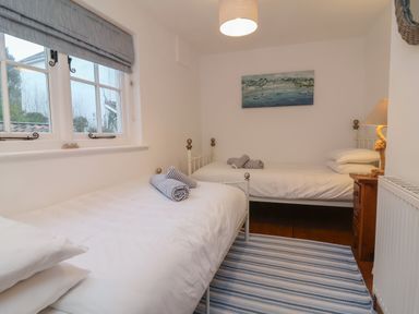 A bedroom with two single beds striped towels a wooden nightstand with a lamp a striped rug and a window at Sunnymead in Bickington near Barnstaple