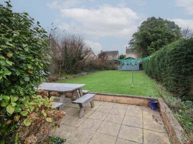 A garden with a wooden picnic table on a patio a rotary clothesline a green lawn and a shed at Sunnymead in Bickington near Barnstaple