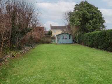 A garden with a lawn a blue wooden shed trees and bushes at Sunnymead in Bickington near Barnstaple