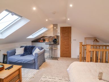 A small living area with a blue sofa, kitchenette with bar stools, wooden railing and bed at The Halt in Maiden Newton