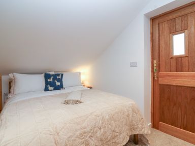 A bedroom with a bed covered by a beige blanket and a wooden door at The Halt in Maiden Newton