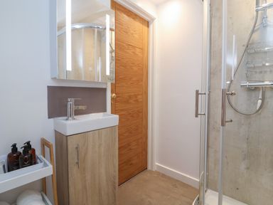 A bathroom with a wooden door a small sink with cabinet and a glass shower enclosure at The Halt in Maiden Newton