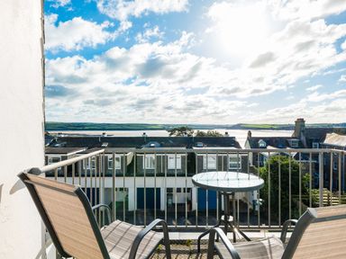 A balcony with two chairs and a glass table overlooking rooftops and water at Slipway 14 in Rock