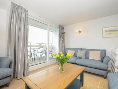 A living room with a blue sofa, armchair, wooden coffee table with yellow flowers, and a balcony with chairs and table at Slipway 14 in Rock
